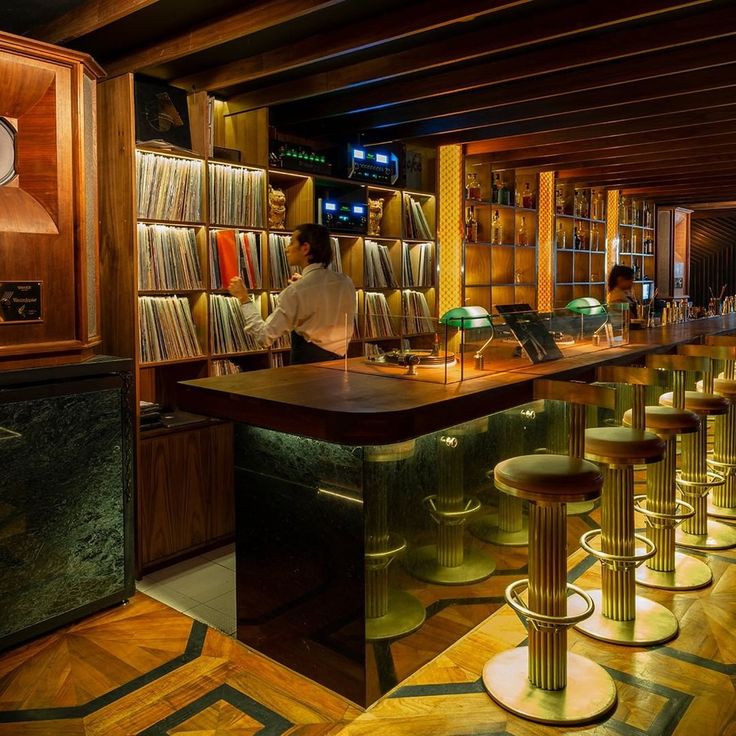 a woman sitting at a bar with lots of books on the shelves and stools