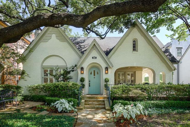 a white house with a blue front door and green shutters on the windows is surrounded by greenery