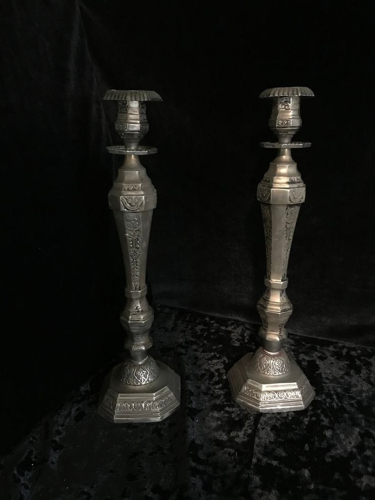 two silver candlesticks sitting side by side on a black tableclothed surface