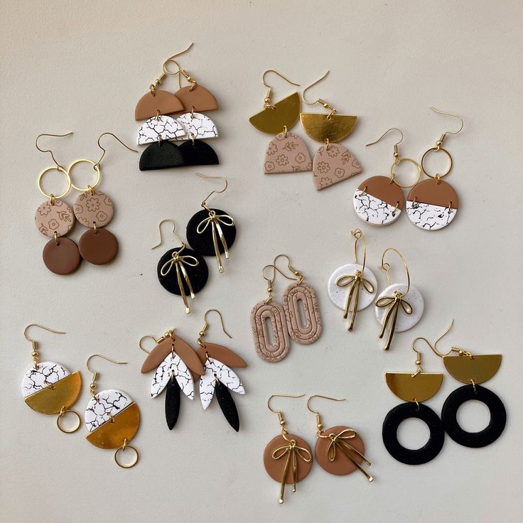 many different types of earrings are arranged on a white surface with gold, black, and brown accents