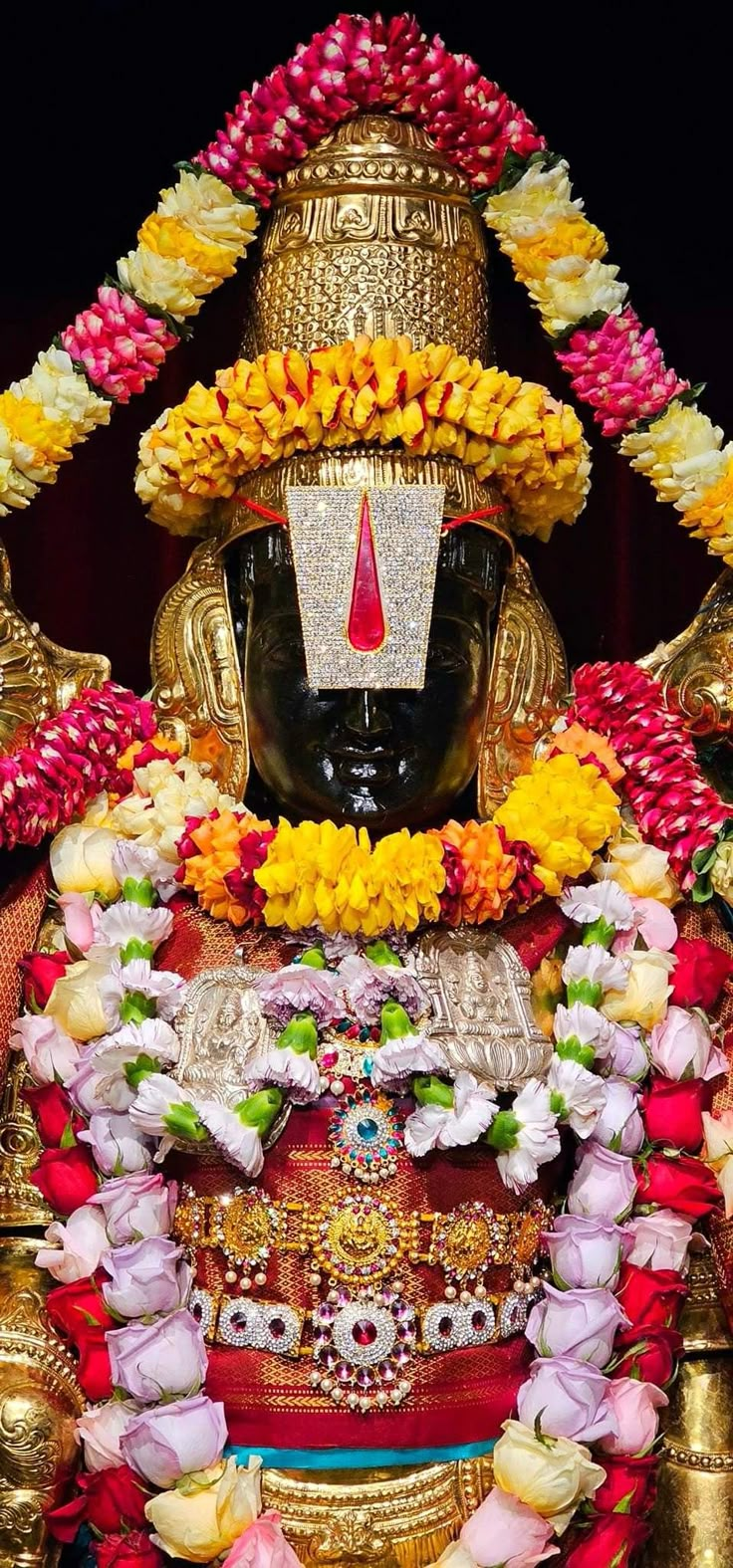 the statue is adorned with flowers and garlands on it's head, in front of a black background