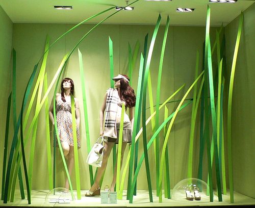 two mannequins dressed in dresses and hats stand behind tall green grass on display