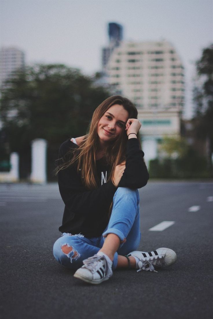 a young woman sitting on the ground with her legs crossed, wearing ripped jeans and a black shirt