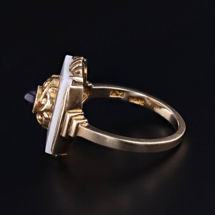 A unique ring featuring an amethyst cabochon atop a white agate backdrop. We created this unique 10k gold ring by riveting the top of an antique shirt stud (circa 1910) onto a 1920s era signet ring. The face of the ring measures 0.7 inches by 0.55 wide, and it is in good condition with some light crazing to the onyx (visible only under magnification). The ring is a size 6.25, but it can be resized free of charge. Materials: 10k gold, Agate, Amethyst. Vintage 14k Stamped Opal Ring For Formal Occasions, Art Deco Oval Cabochon Gemstone Jewelry, Antique Cabochon Sapphire Ring For Formal Events, Vintage Opal Ring With Polished Finish For Formal Occasions, Art Deco Hallmarked Ring With Oval Cabochon, Vintage Signet Ring With Cabochon For Anniversary, Vintage Cabochon Signet Ring For Anniversary, Art Deco Yellow Gold Enamel Ring For Formal Occasions, Art Deco Formal Yellow Gold Enamel Ring