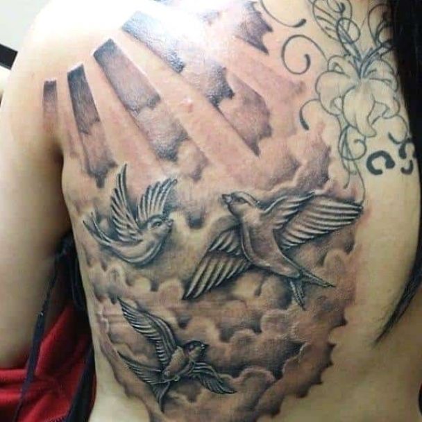 the back of a woman's shoulder with birds flying in the sky and clouds