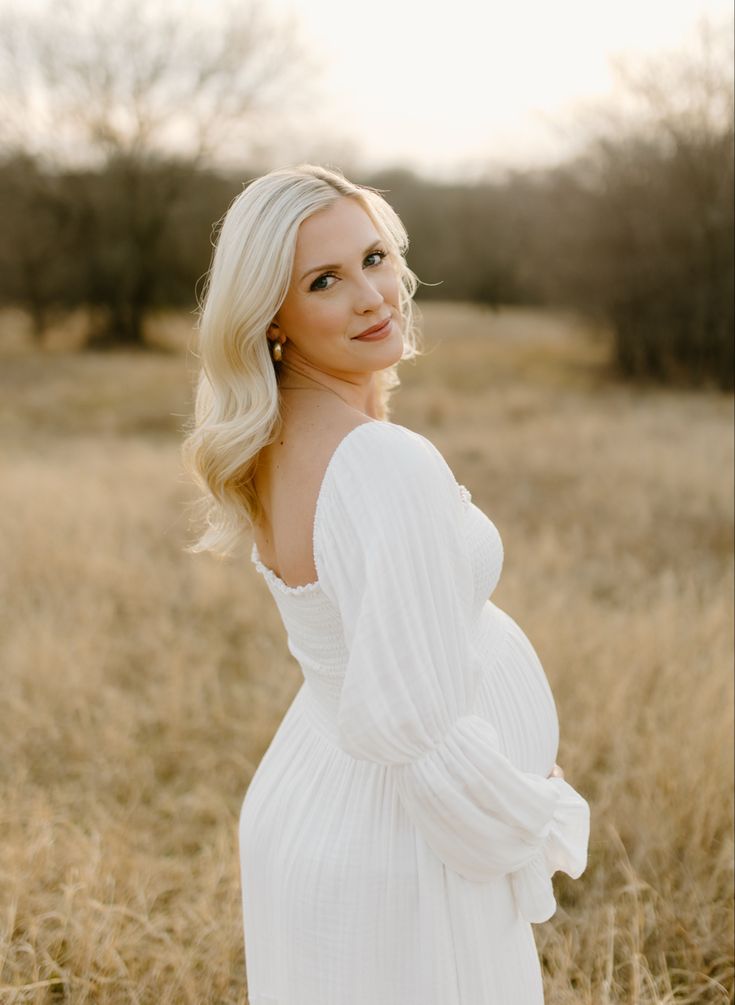 a beautiful blonde woman in a white dress posing for a photo with her hands on her hips