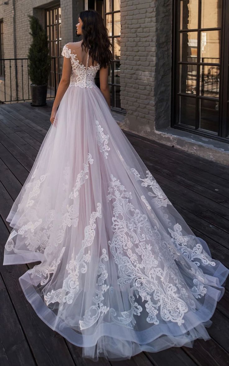 a woman in a wedding dress is standing on a wooden deck with her back to the camera