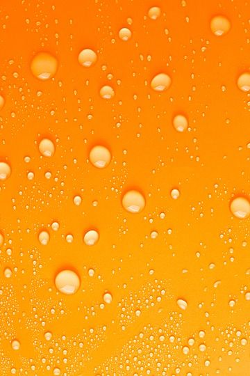 drops of water on the surface of a yellow liquid filled with orange and white bubbles