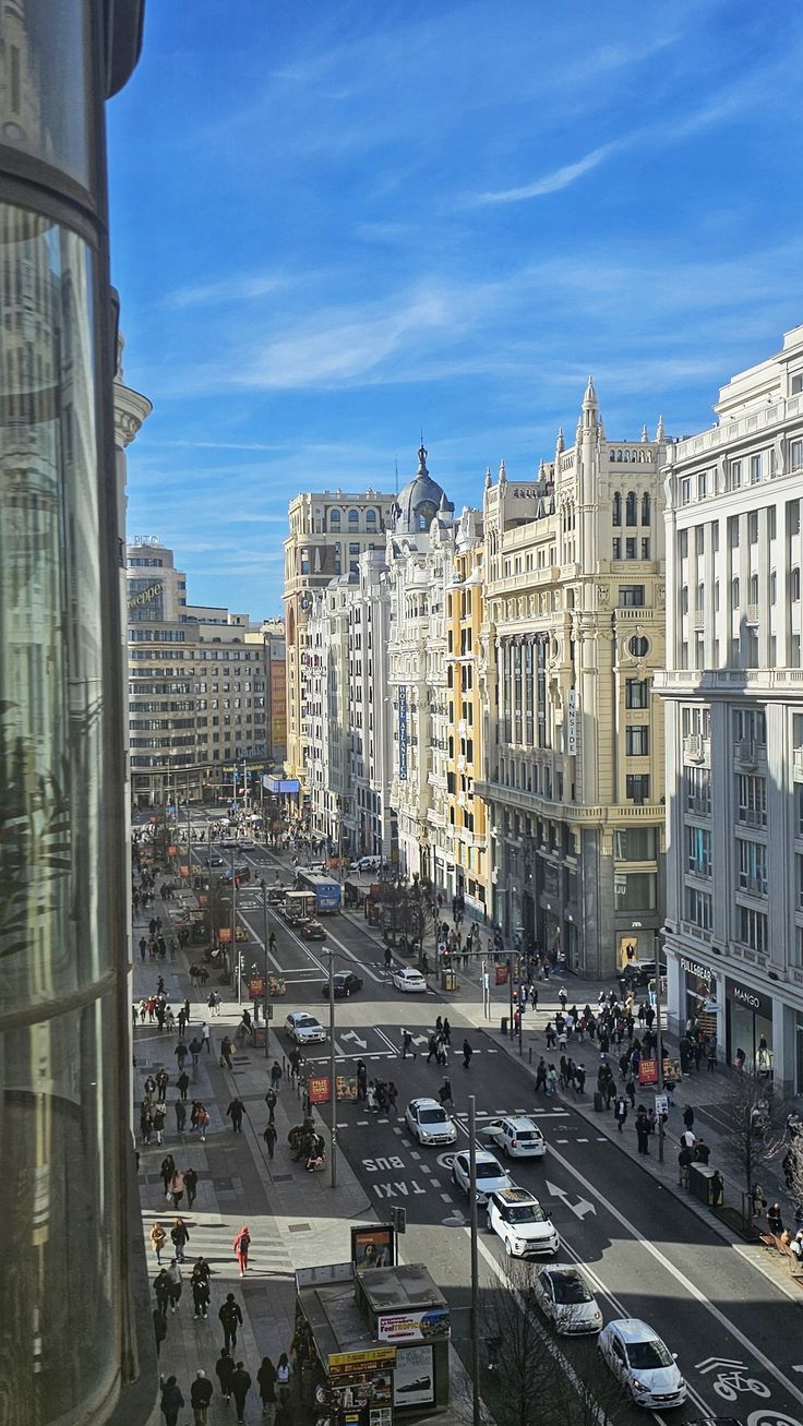 a city street filled with lots of traffic next to tall buildings and people walking on the sidewalk