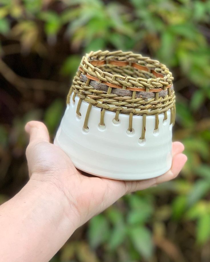 a hand holding a white and brown vase with gold trimmings on it's sides