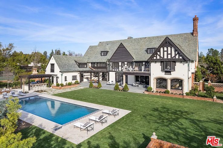 an aerial view of a large house with a swimming pool in the foreground and landscaping surrounding it