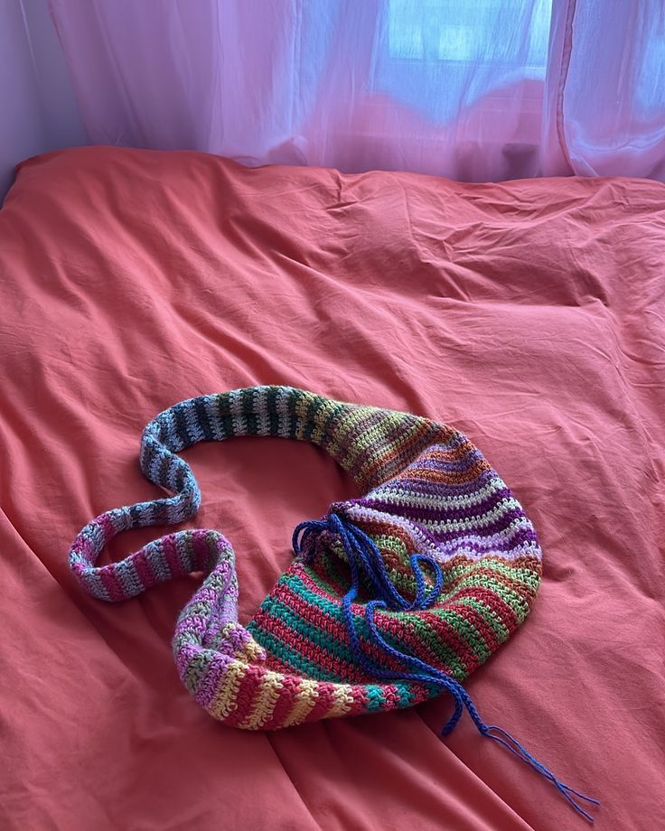 a crocheted bag sitting on top of a bed next to a pink sheet