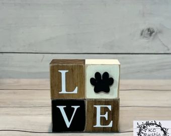 a wooden block that says love with a dog's paw on it and the word love written in black