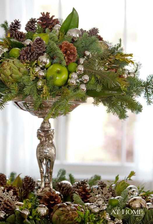 a christmas centerpiece with pine cones, green apples and greenery in a silver bowl