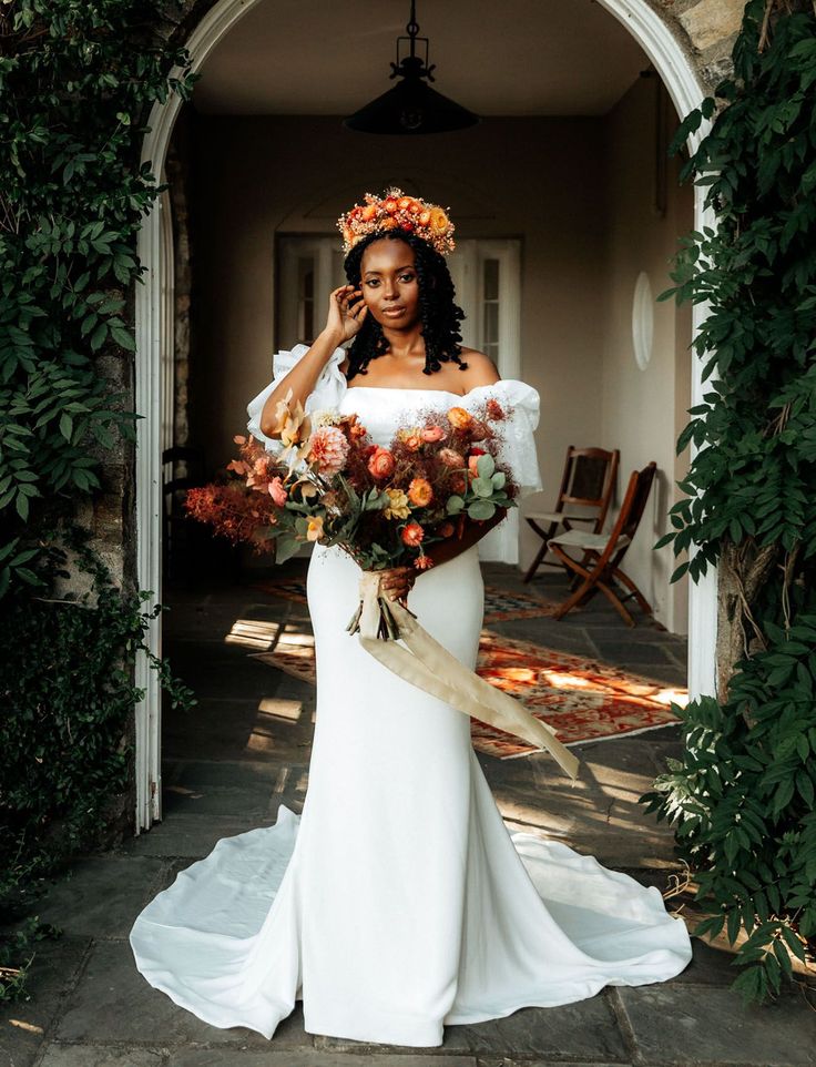 a woman in a white dress holding a bouquet and talking on a cell phone while standing outside