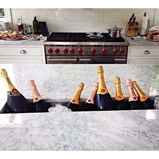 four bottles of champagne are lined up in a row on the kitchen counter top, with gold corks sticking out of them