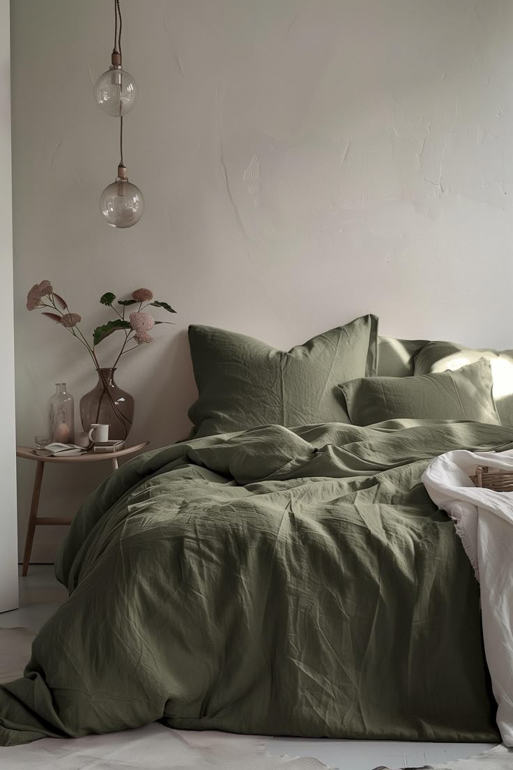 a bed with green sheets and pillows in a room next to a lamp on the wall