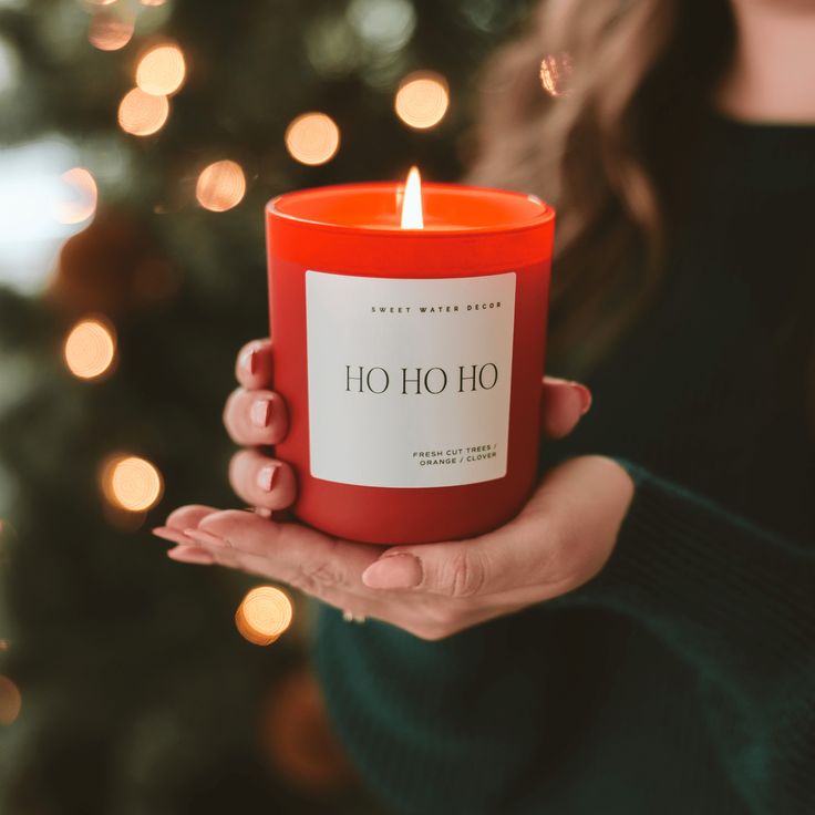 a woman holding a red candle in front of a christmas tree with lights on it