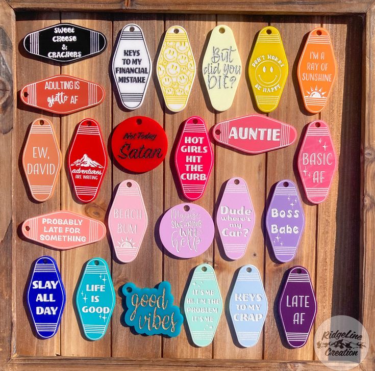 an assortment of different colored tags hanging from a wooden frame on a wood wall with words and phrases