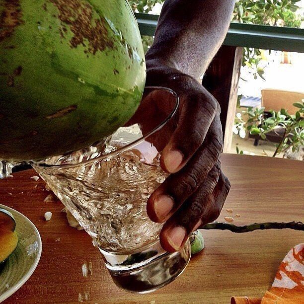 a person pouring water into a glass on top of a wooden table next to fruit