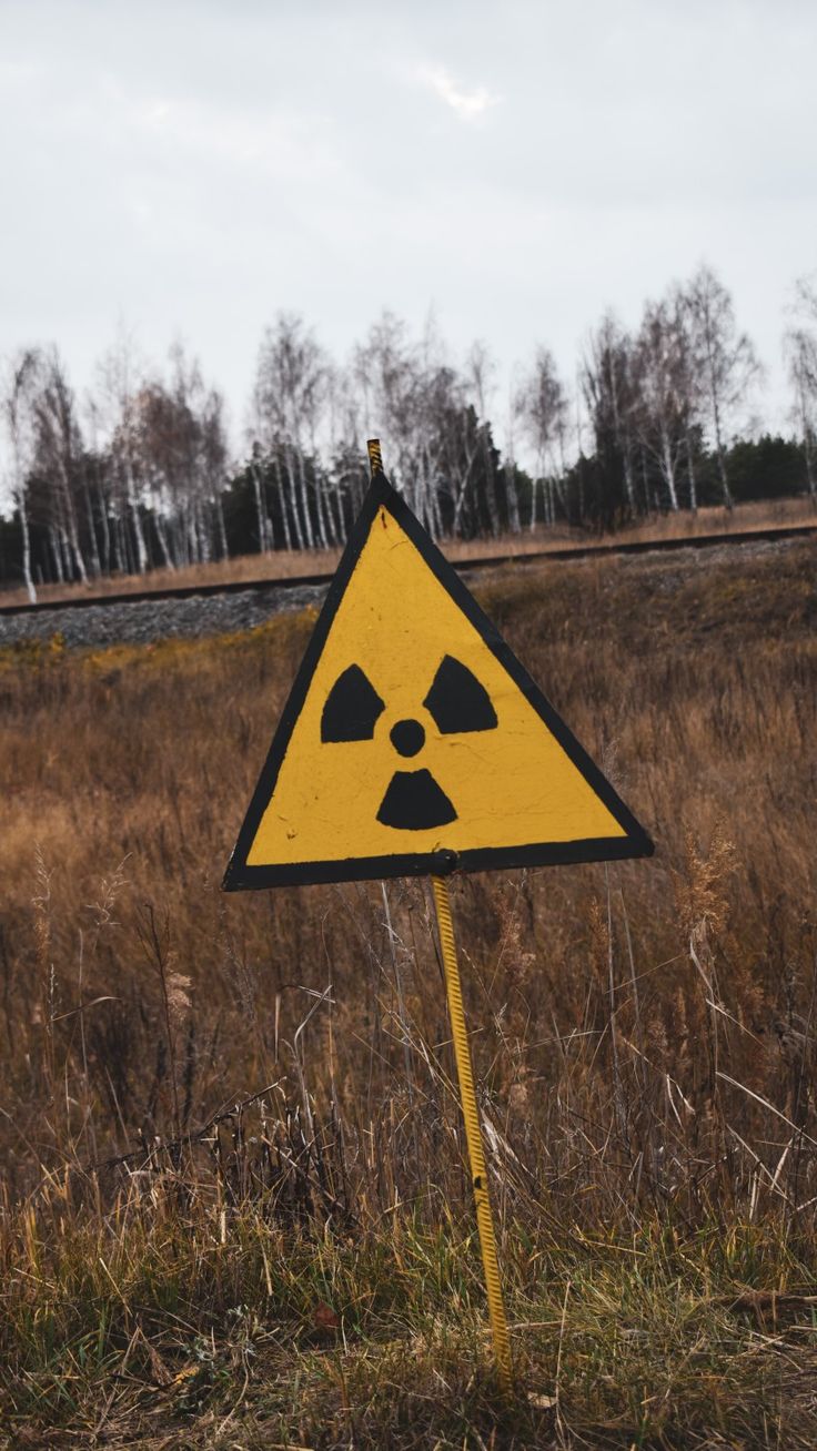 a yellow and black hazard sign sitting on top of a grass covered field