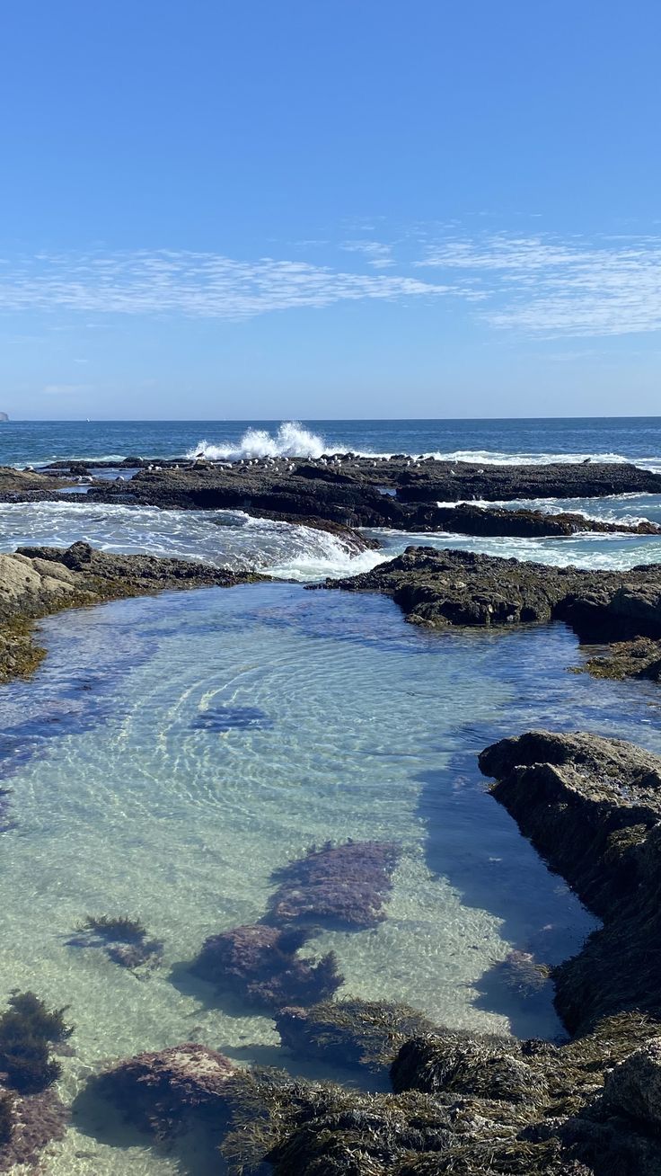 the water is crystal clear and there are rocks on the shore near the ocean with waves coming in