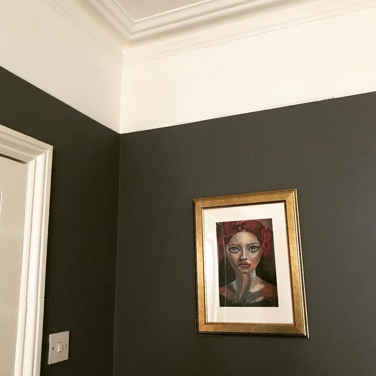 a painting hangs on the wall above a toilet in a bathroom with black walls and white trim