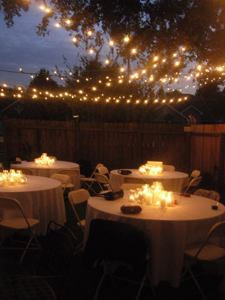 an outdoor dining area is lit up with string lights and white tablecloths set for dinner