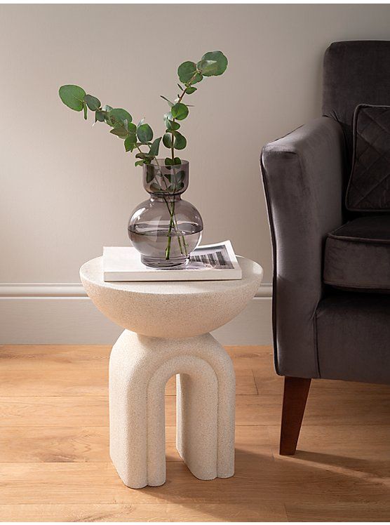 a white table with a plant on it and a gray chair in the corner next to it