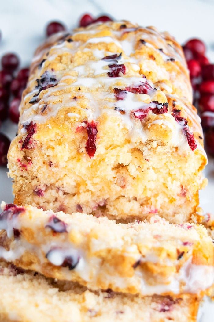 cranberry orange scones with icing on a white plate next to fresh cranberries