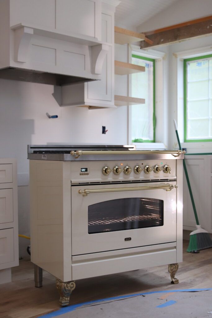 an oven in the middle of a kitchen with white cupboards and drawers on either side