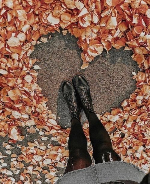 a person standing in front of a heart made of leaves and petals on the ground