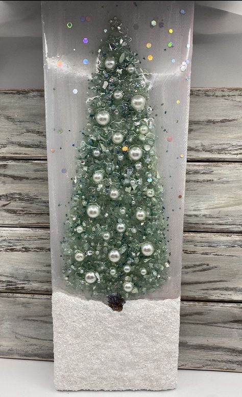 a small white christmas tree in a clear glass container with snow on the bottom and lights around it