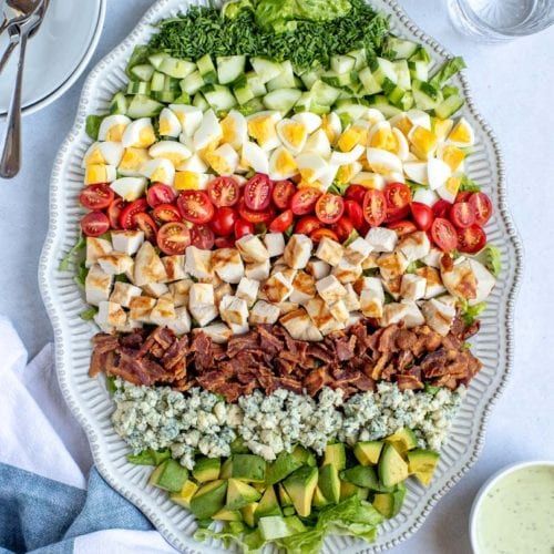 a large platter filled with meat, veggies and dressings on top of a white table