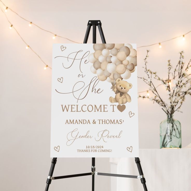 a welcome sign with balloons and a teddy bear on it in front of a string of lights