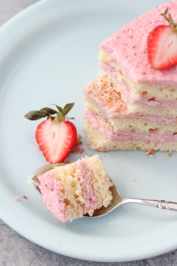 there is a piece of cake with pink frosting and a strawberry on the side