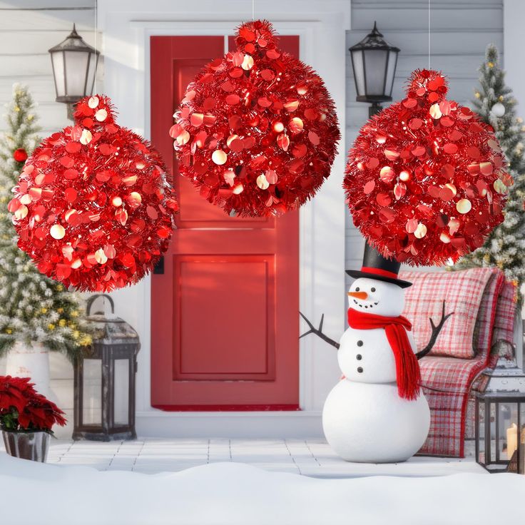 a snowman is standing in front of a red door with two christmas balls hanging from it