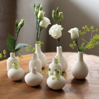 five white vases with flowers in them sitting on a wooden table next to each other