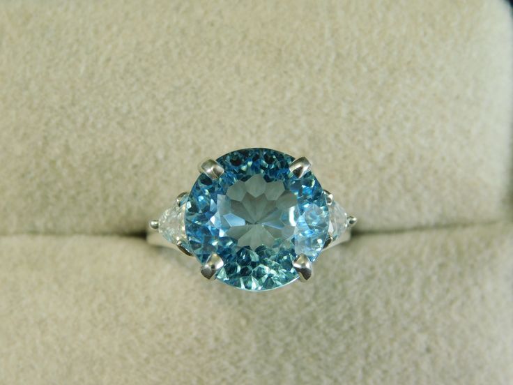 We offer free sizing, free shipping in the USA only, and a free appraisal upon request. If you are an international buyer, please contact us to work out shipping price. Also, we do not pay customs fees. Thanks. November and December Birthstone Sku: MJ1447 This is a 7.04 ct. Round Blue Topaz and Zircon gemstone ring. This is a natural Topaz in a sterling silver setting. The setting also has two .45 ct. clear trillion Zircon accent stones. The ring was hand-crafted in the USA by our staff gemologi Gia Certified Blue Topaz Round Cut Ring, Gia Certified Blue Topaz Ring With Round Cut, Gia Certified Oval Blue Topaz Ring, Blue Trillion Cut Topaz Ring With Accent Stones, Gia Certified Blue Topaz Ring For Anniversary, Blue Trillion-cut Topaz Ring, Blue Topaz Trillion Cut Ring, Blue Trillion Cut Topaz Ring, Gia Certified Blue Topaz Ring In Fine Jewelry Style