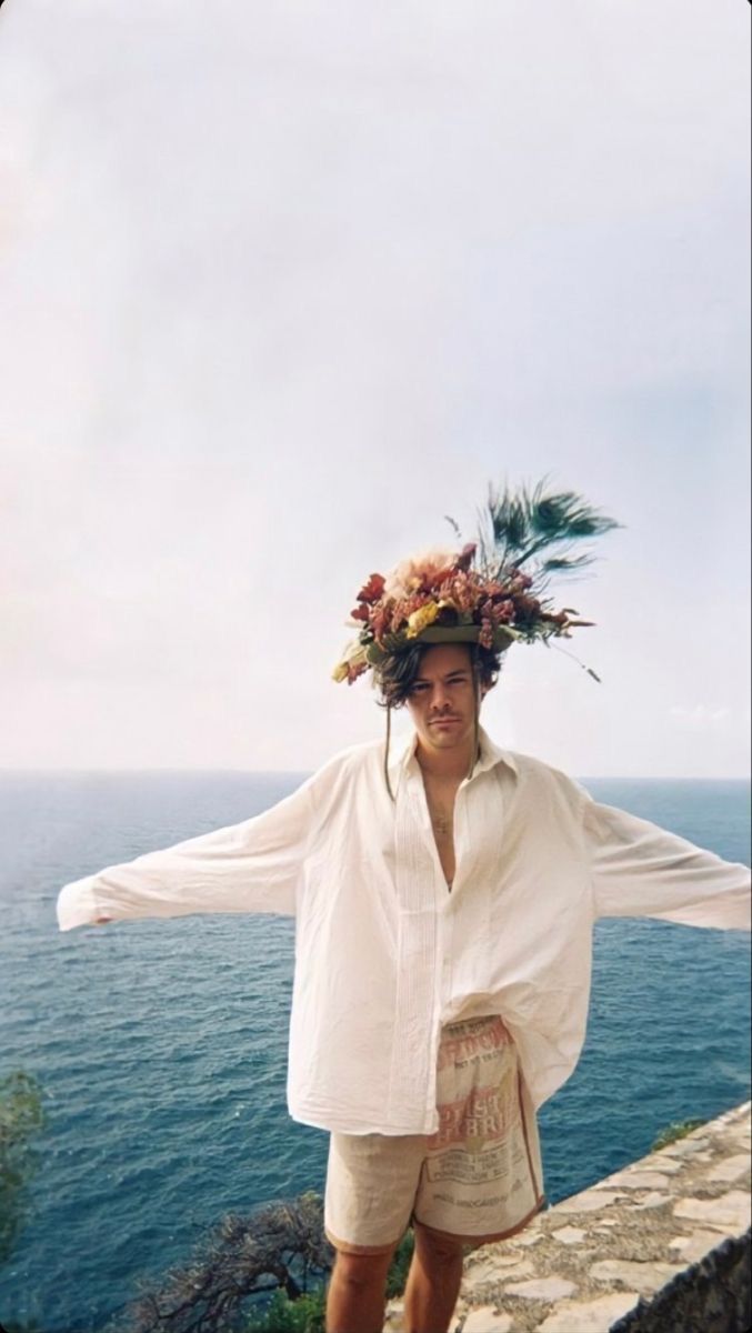 a man with a flower crown on his head standing by the water's edge