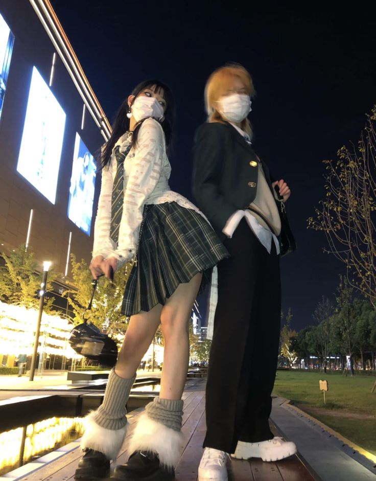 two young women wearing face masks walking down a sidewalk at night with their feet on the ground