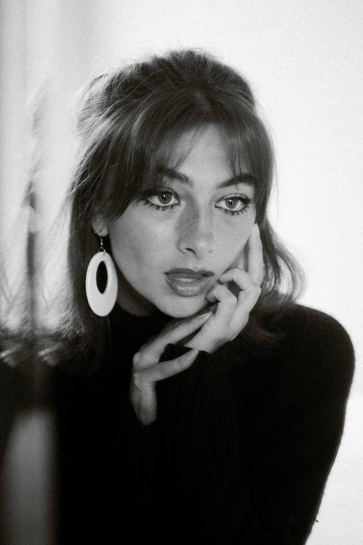 a black and white photo of a woman with her hand on her chin looking at the camera