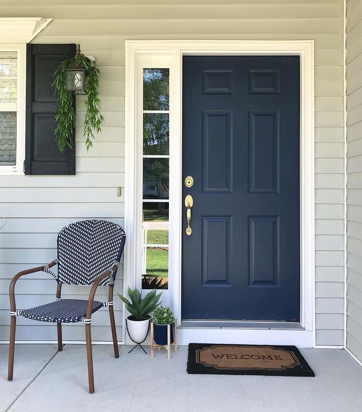 a blue front door with two chairs and a potted plant next to it on the porch