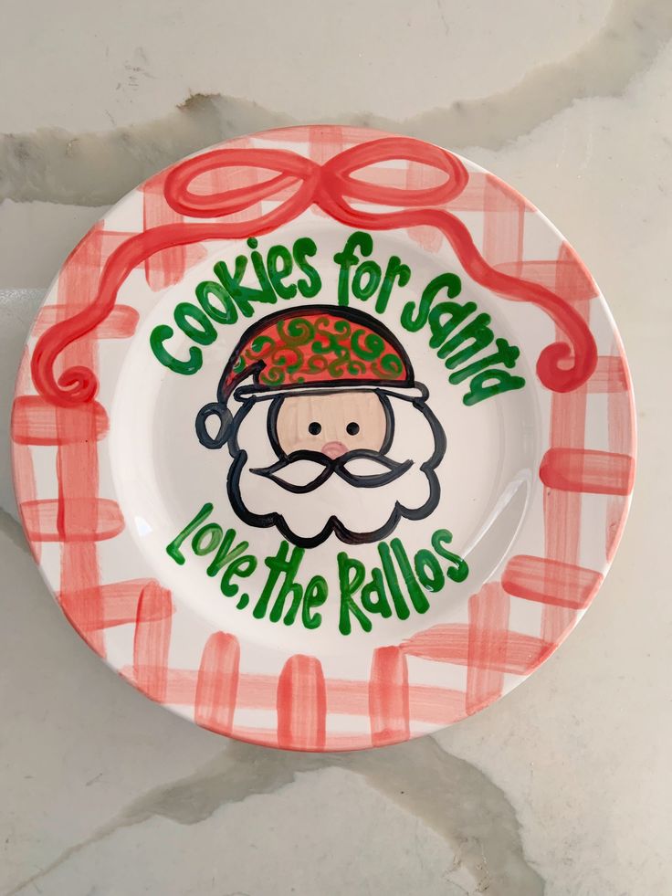 a red and white plate with a cartoon santa clause on it's face that says cookies for santa love the rolls