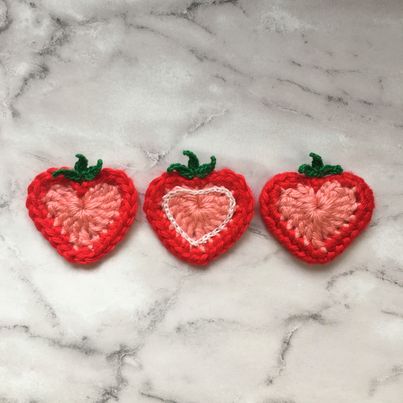 three crocheted strawberries sitting on top of a marble counter