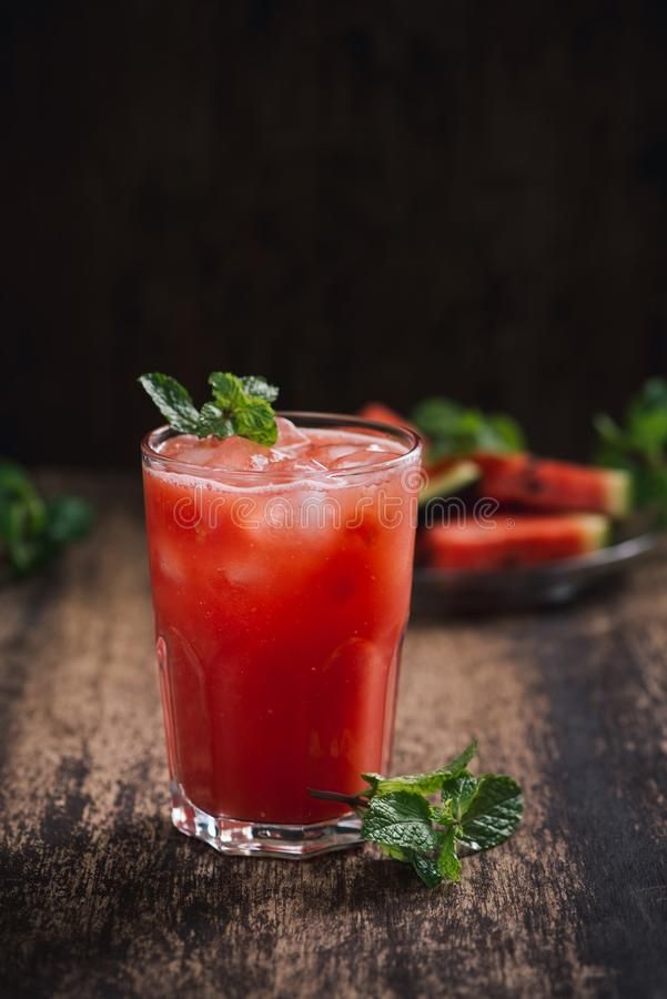 a glass filled with watermelon juice and garnished with mint leaves on a wooden table