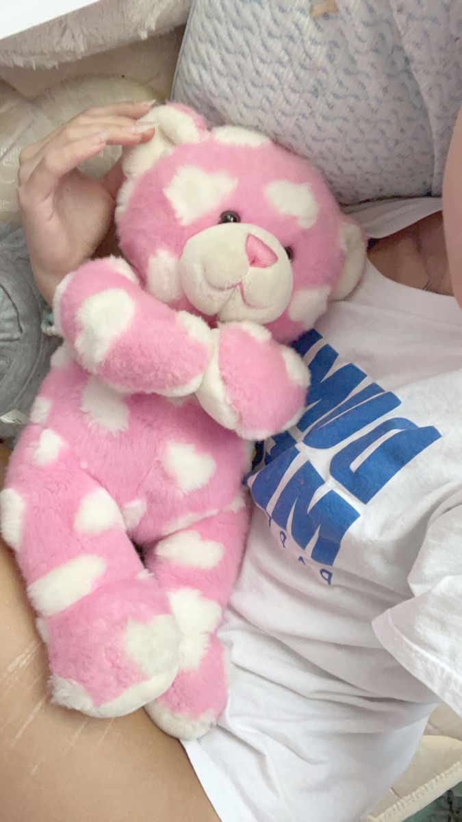 a pink and white teddy bear sitting on someone's lap with his arm wrapped around him