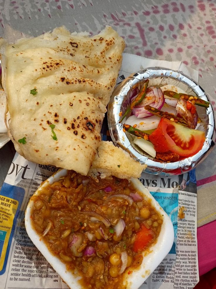 some food is sitting on top of a newspaper next to a bowl of soup and pita bread