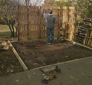 a man standing in the middle of a yard next to a wooden fence and trees