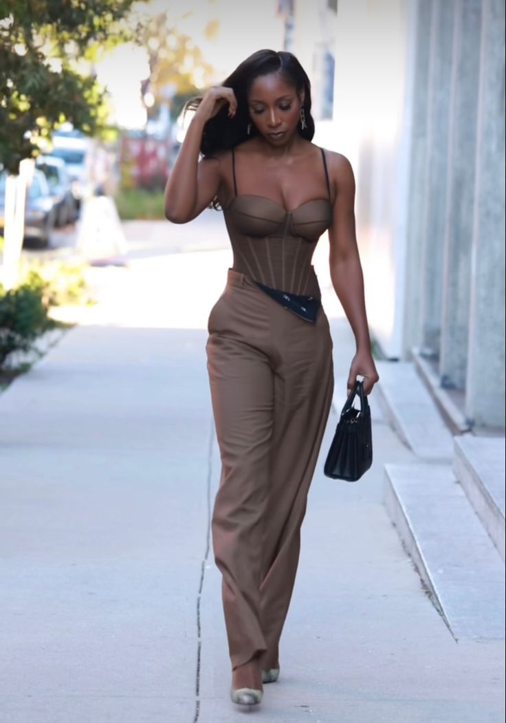 Woman walking in New York wearing a brown corset jumpsuit and a black hand bag Corset Top Jumpsuit, Brown And Gold Outfits For Black Women, Brown Semi Formal Outfits For Women, Black And Brown Dress, Neutral Party Outfit, Corset Jumpsuit Outfit, Nude Corset Outfit, Brown Corset Top Outfit, Nude Outfits For Black Women